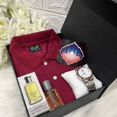 a red shirt and watch in a black box next to white flowers on a bed