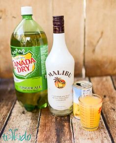 the ingredients to make an alcoholic drink are displayed on a wooden table, including orange juice and ginger ale