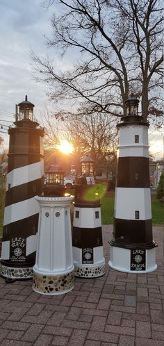 three black and white lighthouses sitting on top of a brick walkway next to a tree