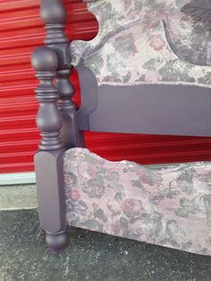 a purple bed frame and foot board with red wall in the background, next to a pink flowered bedspread