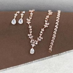 This Rose Gold Floral Bridal Jewelry Set is a perfect ensemble for the bride seeking a touch of boho charm on her special day. The set includes a chunky necklace, teardrop pendent choker, and a leaf bracelet, all adorned with sparkling cubic zirconia stones that catch the light beautifully. CZ NECKLACE: Necklace Length: approx 16 1/2 inches. Featuring a floral design that adds a touch of nature's elegance to your bridal look. Crafted with high-quality cubic zirconia stones and copper, this necklace is designed to sparkle under any light. CZ EARRINGS: These floral design earrings are a beautiful addition to the set, suitable for any occasion. The earring length is about 1 3/8" (3.5cm), with a bottom teardrop size of 1/2"H x 3/8"W (1.5cm x 1cm), offering a delicate balance of size and style. Wedding Jewelry Rose Gold, Bohemian Teardrop Jewelry For Wedding, Bohemian Teardrop Necklace For Weddings, Bohemian Rose Gold Jewelry For Wedding, Rose Gold Teardrop Jewelry Sets For Wedding, Rose Gold Teardrop Wedding Jewelry Sets, Rose Gold Teardrop Bridal Necklace, Bohemian Jewelry Sets With Matching Earrings For Wedding, Bohemian Wedding Necklace With Matching Earrings