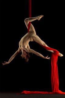 a man is doing aerial acrobatic tricks on a red pole in front of a black background