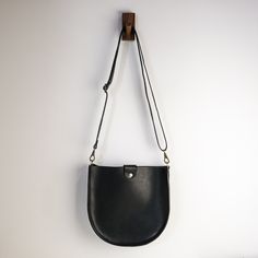 "With a classic saddle bag shape and convenient, magnetic snap closure, this is your new go-to bag. Easily fit everyday items including wallets, keys, phone, and more. We hand-cut buttery soft yet durable 5 oz Horween leather and stitch it with heavyweight nylon thread. The crossbody straps are available in multiple color options and are fitted with solid brass hardware. * Approximately 10\" x 10\" x 2\" * Crossbody strap drop adjusts from 16\" - 28\" * Magnetic snap closure * Unlined interior" Classic Saddle Bag With Adjustable Strap For On-the-go, Classic Crossbody Saddle Bag For On-the-go, Versatile Bucket Bag With Magnetic Closure For Everyday Use, Versatile Everyday Bucket Bag With Magnetic Closure, Leather Crossbody Bucket Bag With Magnetic Closure, Top Handle Bag With Magnetic Closure, Minimalist Crossbody Shoulder Bag With Magnetic Closure, Rectangular Saddle Bag With Magnetic Closure For Daily Use, Saddle Bag With Detachable Strap For Everyday Use