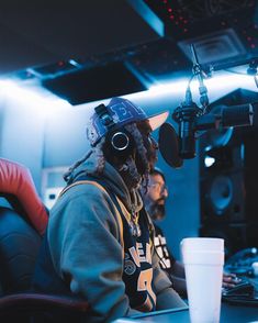 two people sitting at a table with headphones on and one person wearing a hat