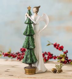 a ceramic figurine holding a star next to a christmas tree on a table