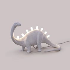 a white toy dinosaur with lights on its head and neck, standing in front of a gray background