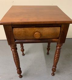 an old wooden table with turned legs and a drawer on one side, sitting in a room