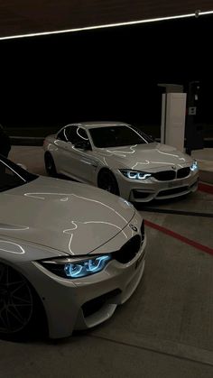 two white cars parked next to each other in a parking lot at night with the lights on