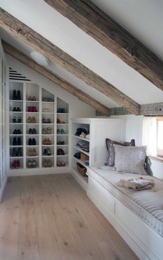 an attic bedroom with white walls and wooden flooring, built in shelving units filled with shoes