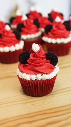 some cupcakes with red frosting and mickey mouse ears on top are sitting on a table