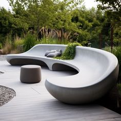 a curved bench sitting on top of a wooden floor next to a lush green forest