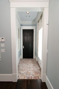 an empty hallway with a black door and brick flooring on the side by side