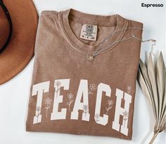 a brown t - shirt with the word teach on it next to a straw hat