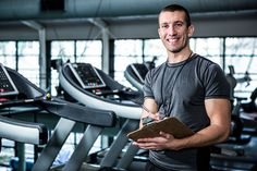 a man standing in front of a row of treadmills holding a clipboard