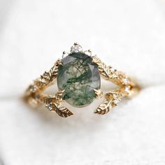 This exquisite Moss Agate ring set features the serene beauty of nature captured in elegant simplicity. Crafted with care, it showcases the captivating charm of moss agate, a stone renowned for its lush green hues and intricate patterns reminiscent of verdant forests. The delicate leaf motif adorning the band adds a touch of organic grace, enhancing the ring's natural charm. Nature-inspired Rings With May Birthstone Gemstone, Nature-inspired Gemstone Rings For May Birthstone, Nature-inspired Rings With May Birthstone, Nature-inspired Oval Agate Jewelry, Elegant Oval Moss Agate Rings, Nature-inspired Wedding Rings With Natural Stones, Elegant Moss Agate Rings With Natural Inclusions, Moss Agate Ring With Natural Stones, Nature-inspired Moss Agate Jewelry With Natural Inclusions