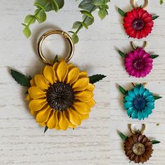 four flower keychains are arranged on a white table with green leaves and flowers