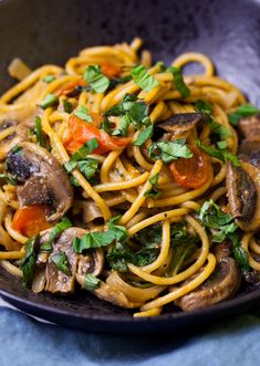 pasta with mushrooms, carrots and parsley in a black bowl on a blue cloth