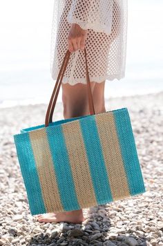 a woman carrying a blue and beige striped bag on the beach with her feet in the sand