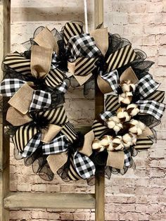 a black and white wreath with burlucks hanging on a ladder next to a brick wall