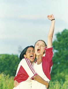 two young women are hugging and smiling while they hold their arms up in the air