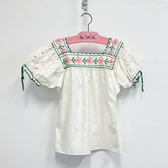 Vintage Childs embroidered peasant top featuring; a square neckline both front and back short pouffy sleees with  a drawsting at the cuff cut straight across the bottom the neckline is embroidered with cross stitched flowers Of a smooth light weight cotton in a crisp white, the embroidery is emerald green, a corally pink, and a darker pink. With no labels or tags, measurements when laid out flat are; 15 inches pit to pit 6 inch sleeve 16 1/4 inches across the bottom 19 1/4 inches from shoulder t Embroidered Peasant Top, Casual Floral Embroidery Square Neck Top, Casual Floral Embroidered Square Neck Top, Bohemian Peasant Top With Smocked Bodice, Casual Square Neck Top With Floral Embroidery, Bohemian White Square Neck Tops, Cotton Floral Embroidery Square Neck Top, Spring Bohemian Blouse With Square Neck, Cotton Top With Floral Embroidery And Square Neck