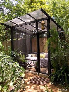 a small glass house in the middle of some plants and trees with a bed inside