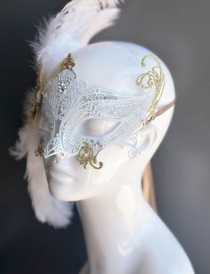 Our women's white laser cut metal masquerade mask, adorned with delicate white feathers and a gold crystal brooch, offers you the opportunity to add a touch of enchanting gold glitter to the mask. Whether you're attending a grand masquerade ball, a themed gala, or simply looking to add a touch of elegance to your attire, this mask ensures you'll be the center of attention. Age Group/Gender - Adult/Women Size/Type - One size fits all adults Mask Color - White Mask Material - Laser cut metal Gold And White Masquerade Mask, Dove Mask Masquerade, Masquerade Mask With Veil, Angel Mask Masquerade Ball, Elegant White Masquerade Mask For Carnival, Elegant White Masquerade Mask For Mardi Gras, White Eye Mask For Masquerade, White Masks For Carnival Party, Elegant White Eye Mask