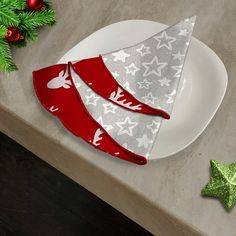 two christmas napkins on a white plate next to green and red decorations with silver stars