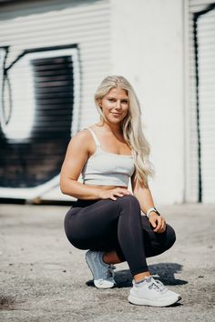 a woman squatting on the ground in front of a building with graffiti painted on it