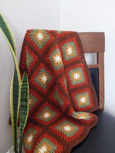 a crocheted blanket sitting on top of a chair next to a potted plant