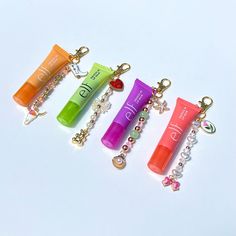 four different colored tubes with charms attached to them on a white surface and one is holding a keychain