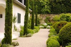 a house with lots of trees and bushes around it's perimeter, along with a gravel path leading to the front door