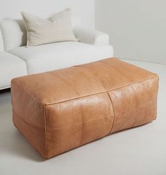 a tan leather ottoman sitting on top of a white floor next to a couch and pillows