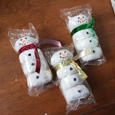 four snowman marshmallows wrapped in cellophane on a wooden table