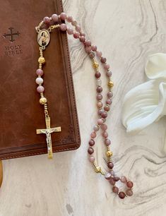 "\"If every tiny flower wanted to be a rose, spring would lose its loveliness.\" - St. Therese of Lisiuex Our beautiful new \"Little Flower\" handmade Rosary reminds us that God has created us each uniquely in His image to share our gifts of love with the world. Saint Thérèse is known as the Saint of the Little Ways, meaning she believed in doing the little things in life well and with great love. She is represented by roses. May everyone who receives this rosary be blessed. Crafted with - 8mm Natural Strawberry Quartz beads - 9mm Gold Acrylic Rose Beads - 2inch Gold With Silver tone Jesus Crucifix - Saint Therese Of Lisieux  Rosary Centers" Rosary Ideas, Sacred Space Altar, Chaplet Rosary, Acrylic Rose, Spiritual Faith, Saint Therese, In His Image, Handmade Rosary, Rose Beads