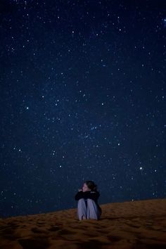 a person sitting on top of a sandy hill under the stars