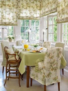 a dining room table covered in green cloths and chairs with flowers on the valance