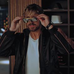 a man is looking through his sunglasses while standing in front of a bookcase and shelves