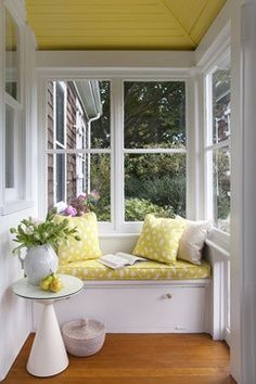 a white window seat sitting under a yellow painted skylight next to a table with flowers on it