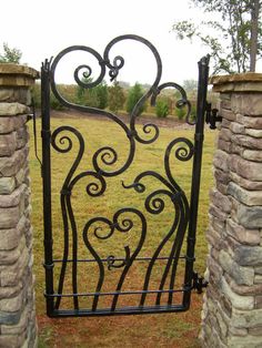 an iron gate in the middle of a grassy area with stone pillars on either side