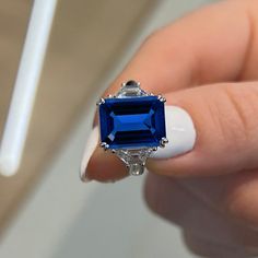 a woman's hand holding a ring with an emerald and blue stone in it