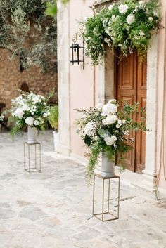 two tall vases with flowers on stands in front of an old stone wall and door