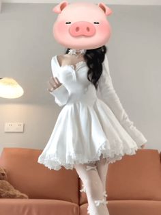 a woman in a white dress with a pig mask on her head, standing next to a couch