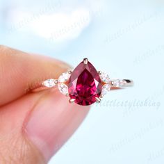 a woman's hand holding a ring with a pink stone and two white diamonds