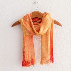 an orange and red scarf hanging on a white wall next to a wooden hanger