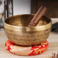 a golden singing bowl sitting on top of a red pillow next to a wooden mallet