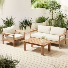 two couches and a coffee table on a deck with potted plants in the background