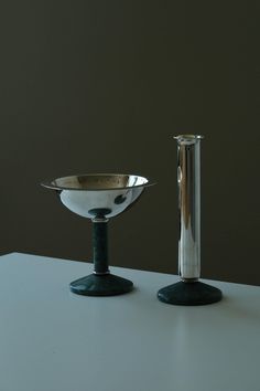 two silver vases sitting next to each other on a white counter top with a black base