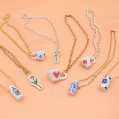 several necklaces with different designs on them sitting on a pink surface, one has a gold chain and the other is white