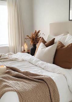 a bed with pillows, blankets and candles on top of it in front of a window